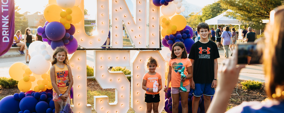 Four children pose in front of a UNI 150 sign while having their photo taken at Homecoming 2025