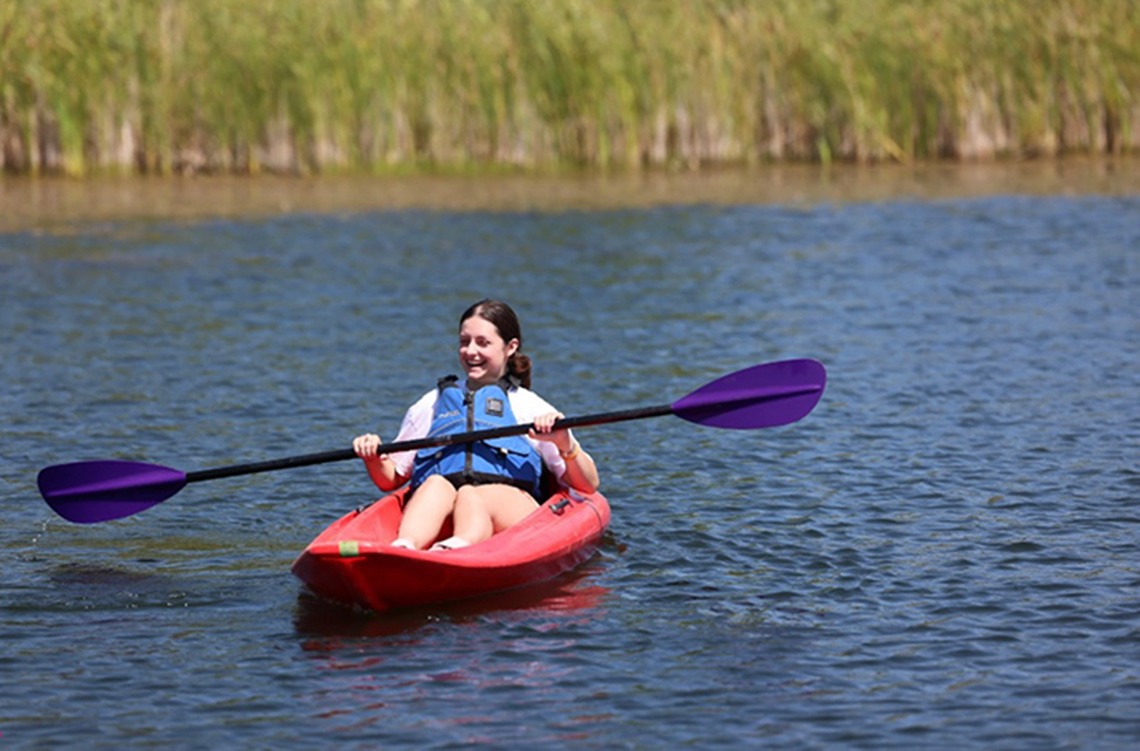 A lake scenery with a girl on a red paddle smiling