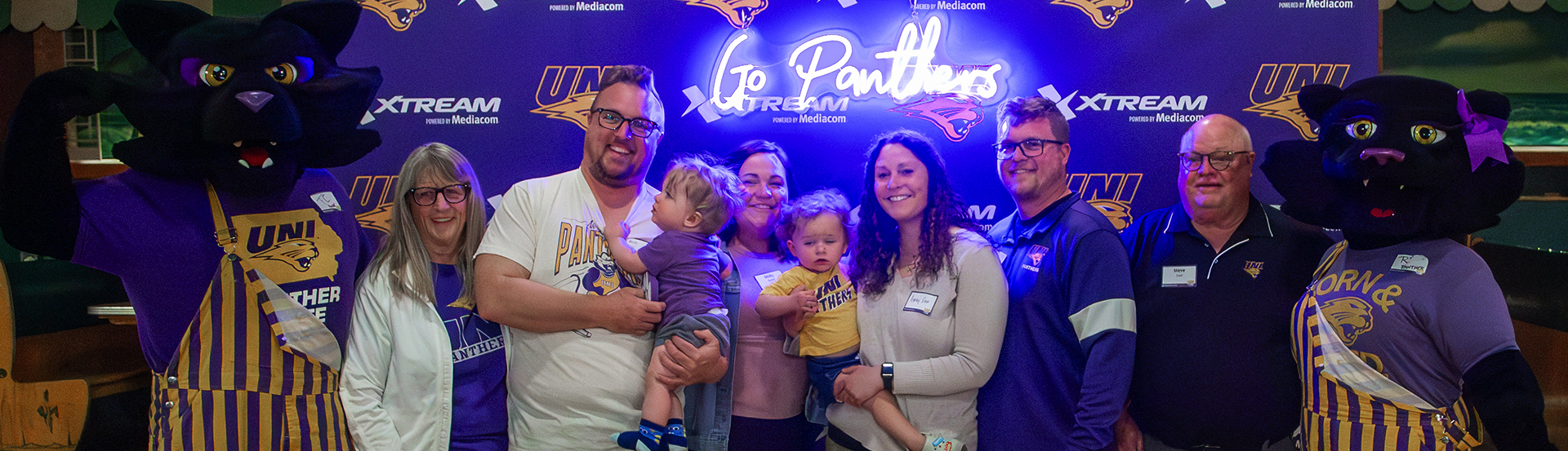 A family poses with TC & TK in front of a backdrop that reads, "Go Panthers"