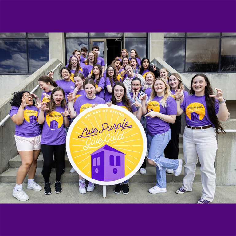Connecting Alumni to Students (CATS) organization making silly poses and cheering with a giant #LivePurpleGiveGold sign