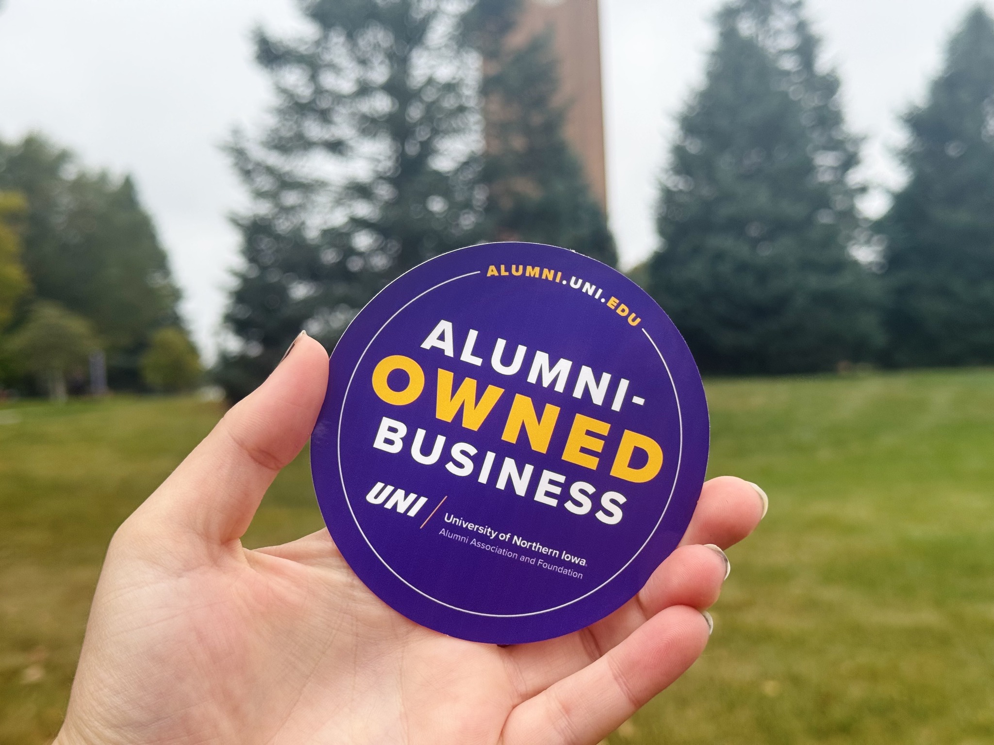 Person holding an alumni owned business purple sticker