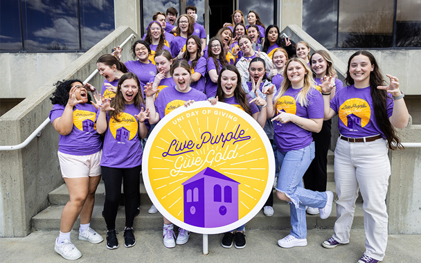 Alumni Association Student Organization, Connecting Alumni to Students, group posing with a large #LivePurpleGiveGold sign