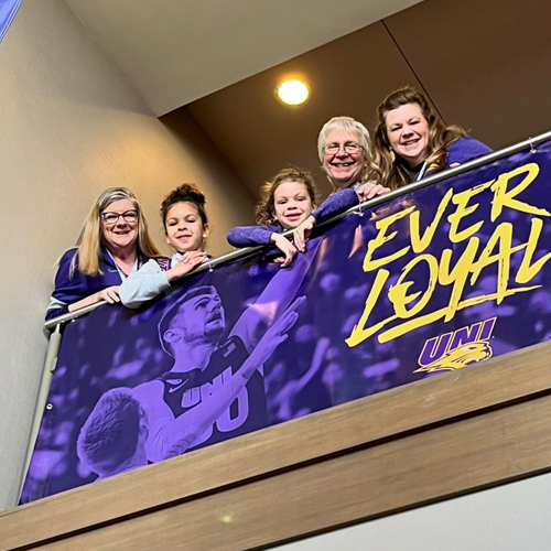 Five Panther fans of all ages watch the action below over the balcony of the hotel which displays an EverLoyal UNI baskeball banner