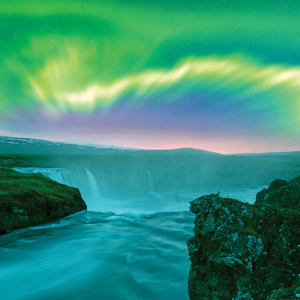 Bright green Northern Lights shine over a blue rushing river and waterfalls in Iceland