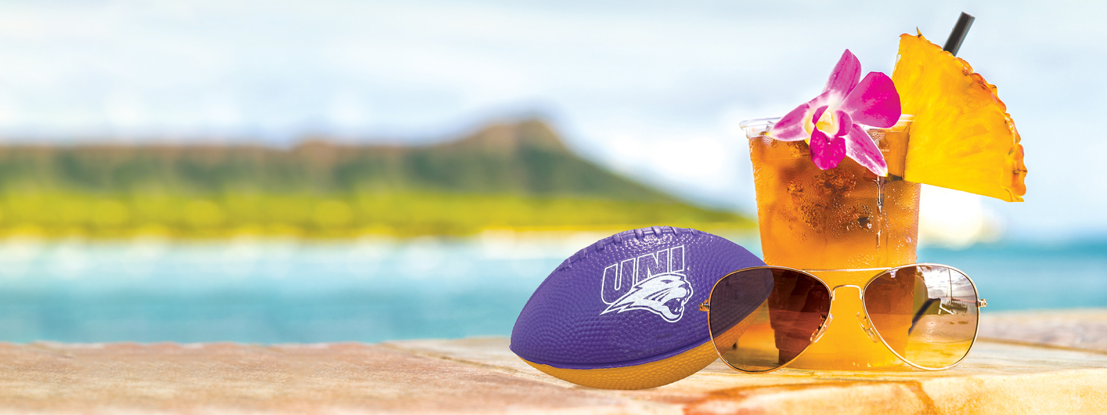 UNI foam football next to a tropical drink and sunglasses with a Hawaiian backdrop 
