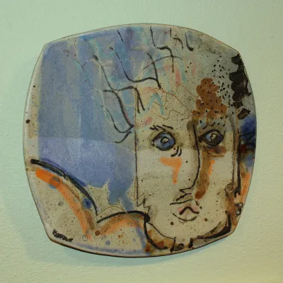 Decorative ceramic plate with abstract face design in blue and orange tones